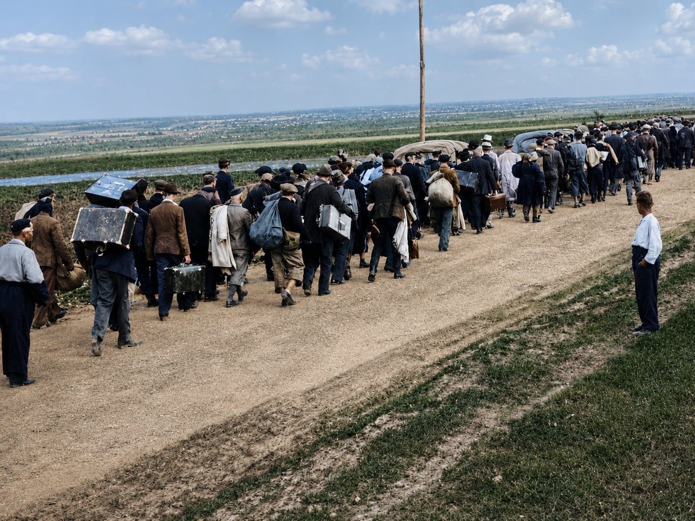 A long column of Polish civilian refugees on a country road, carrying suitcases and bundles as they walk away from the camera towards the Romanian border, September 1939. Colourised period photograph.